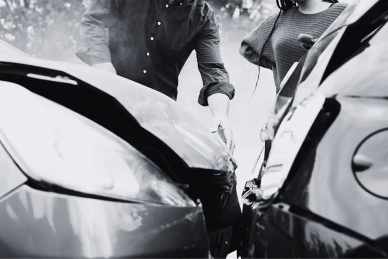 two cars in front end collision and drivers standing by car looking at damage